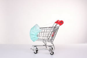 A shopping cart is covered by a large mask, which sits over the front of the cart, with the straps attached to the handlebars. This is to represent stores taking precautions and making changes for the pandemic. It does this by putting a mask on the symbol of shopping, just as we would put a mask on ourselves.