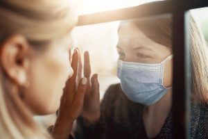 two women separated by glass and masks